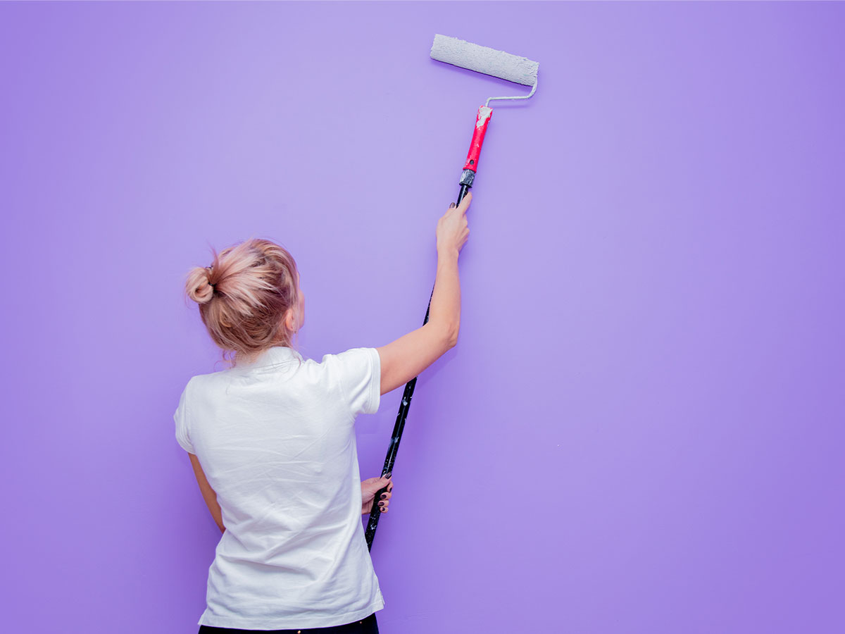 Woman holding an extendable paint roller to paint a wall lavender